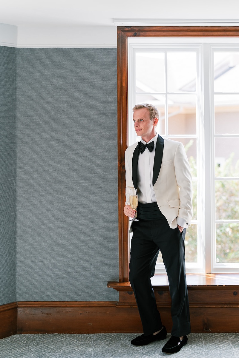 Groom in white tuxedo jacket holds champagne glass. Elegant wedding at the Ritz-Carlton Lake Oconee in Georgia. Sarah Bradshaw Photography.