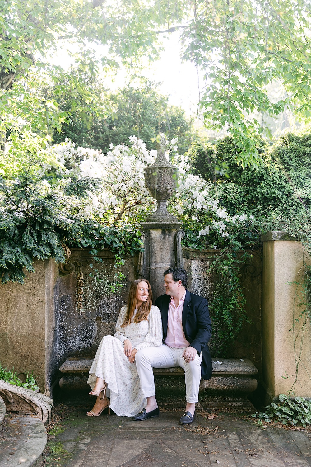 Couple sits on garden bench. Spring wedding engagement photo session. Sarah Bradshaw Photography.