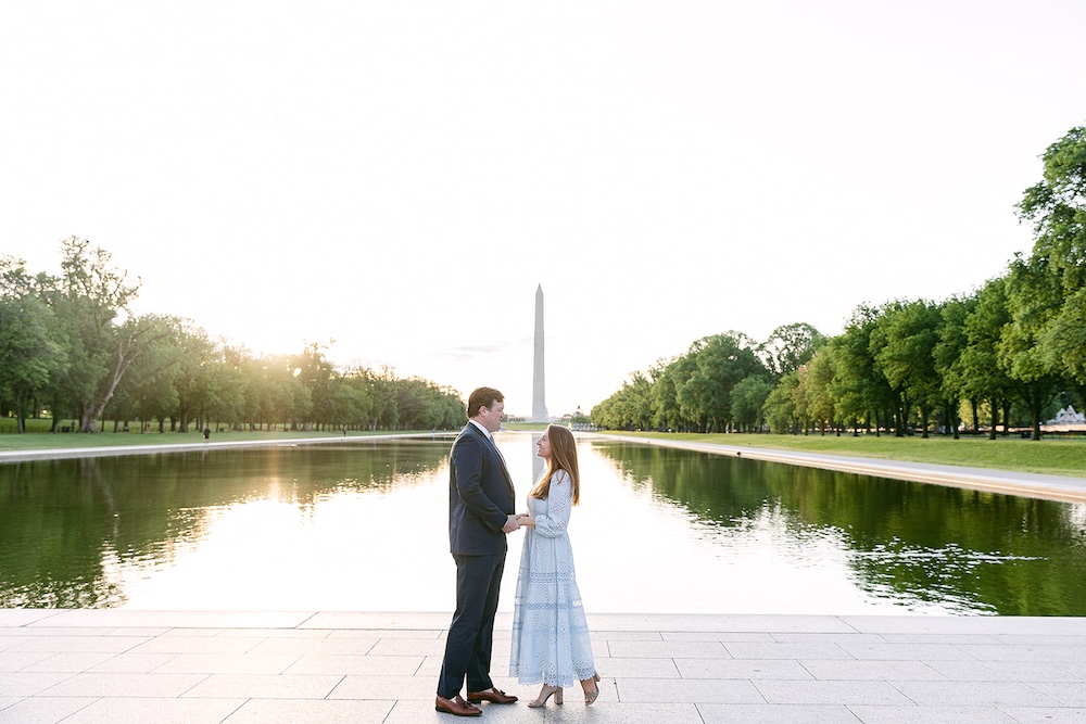 Couple poses in front of DC reflecting pool at sunset with Washington Monument behind them. Spring wedding engagement photo session. Sarah Bradshaw Photography.