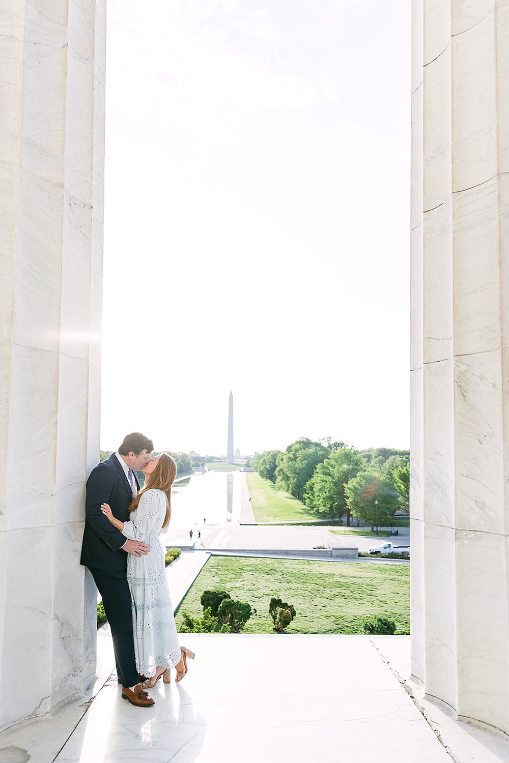 Couple kisses at the Lincoln Memorial with Washington Monument in the background at sunset. Spring wedding engagement photo session. Sarah Bradshaw Photography.