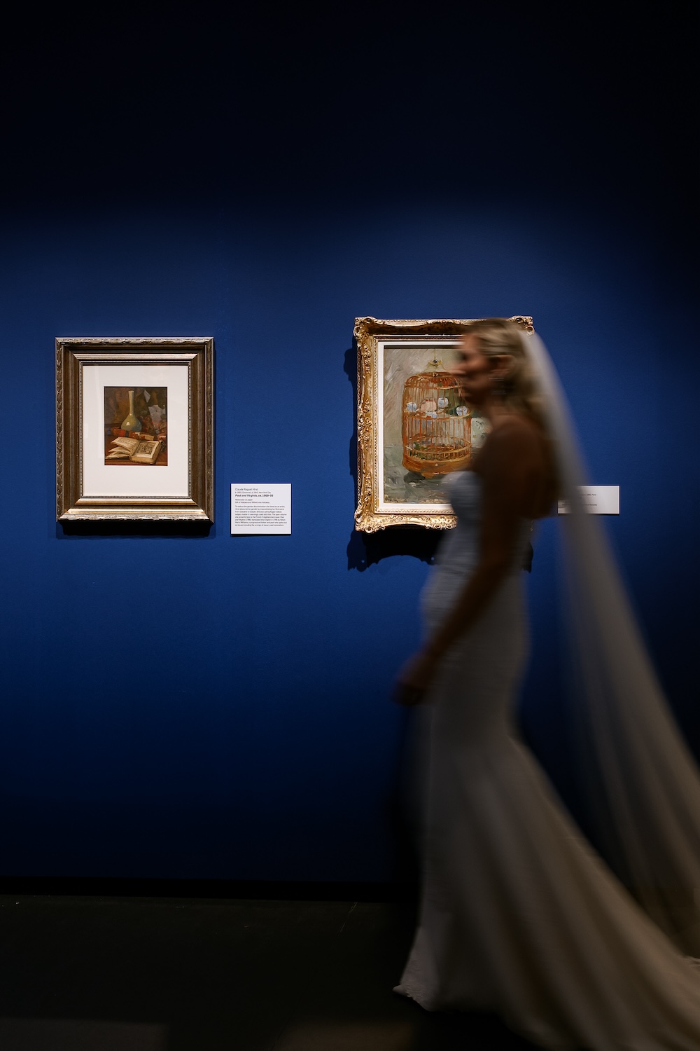 In motion photograph, bride walks past hanging artwork in museum. Modern Washington DC wedding at National Museum of Women in the Arts. Sarah Bradshaw Photography.