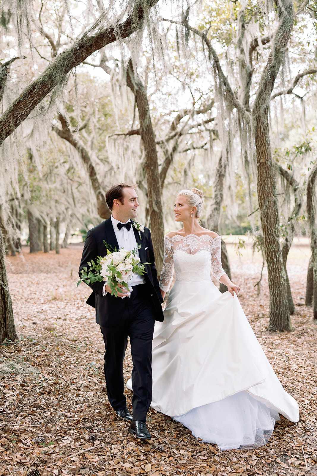 Portrait of bride and groom walking in grove of live oak trees. Classic Black Tie wedding in Georgetown, SC. Sarah Bradshaw Photography