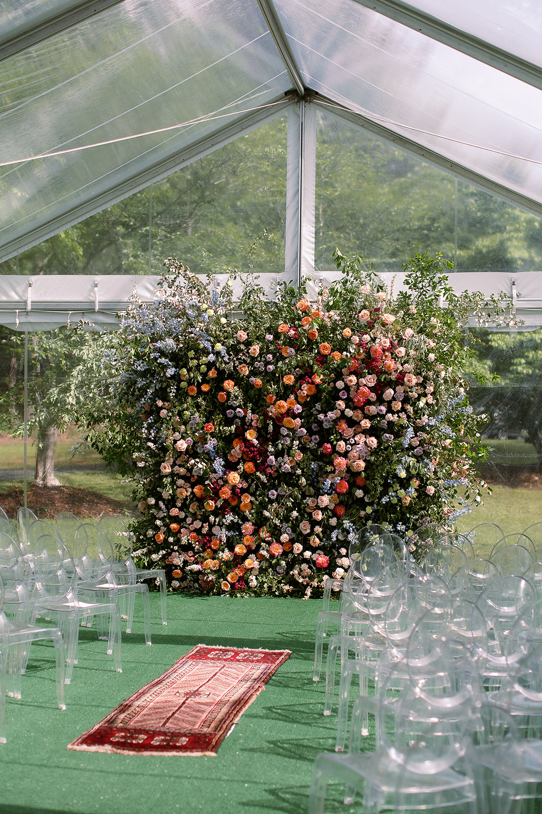 Lush, colorful floral wedding ceremony backdrop wall. clear chairs, tented wedding ceremony. at home wedding in south carolina. Sarah Bradshaw Photography