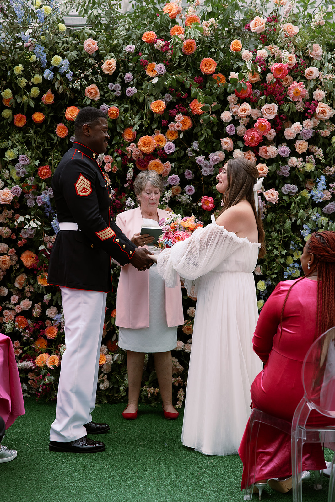bride and groom hold hands in front of colorful floral ceremony backdrop. Spring, private home tented wedding in south carolina. Sarah Bradshaw Photography