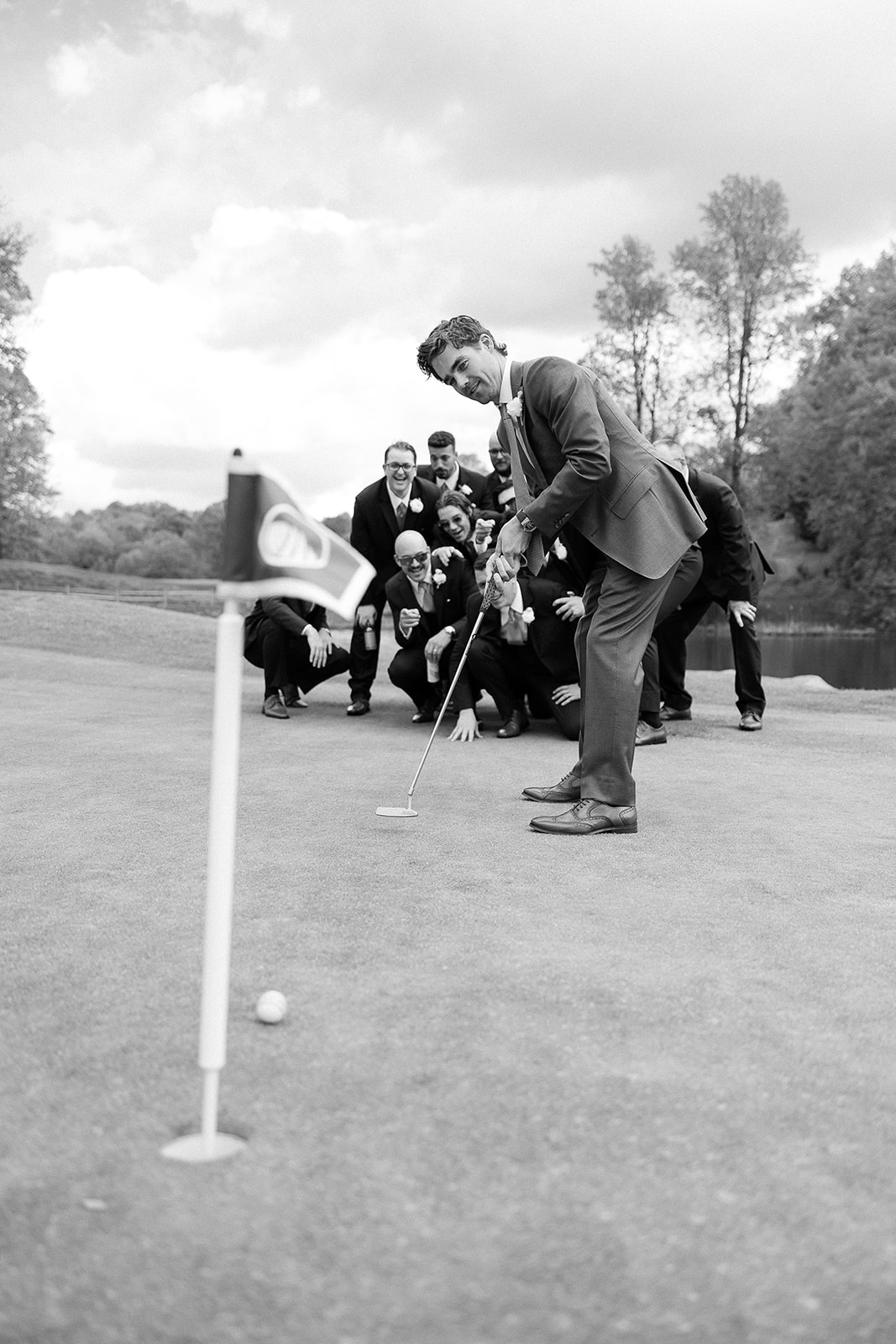 creative groom portrait, groomsmen in background. groom putting ball on golf course. elegant south carolina spring wedding. sarah bradshaw photography