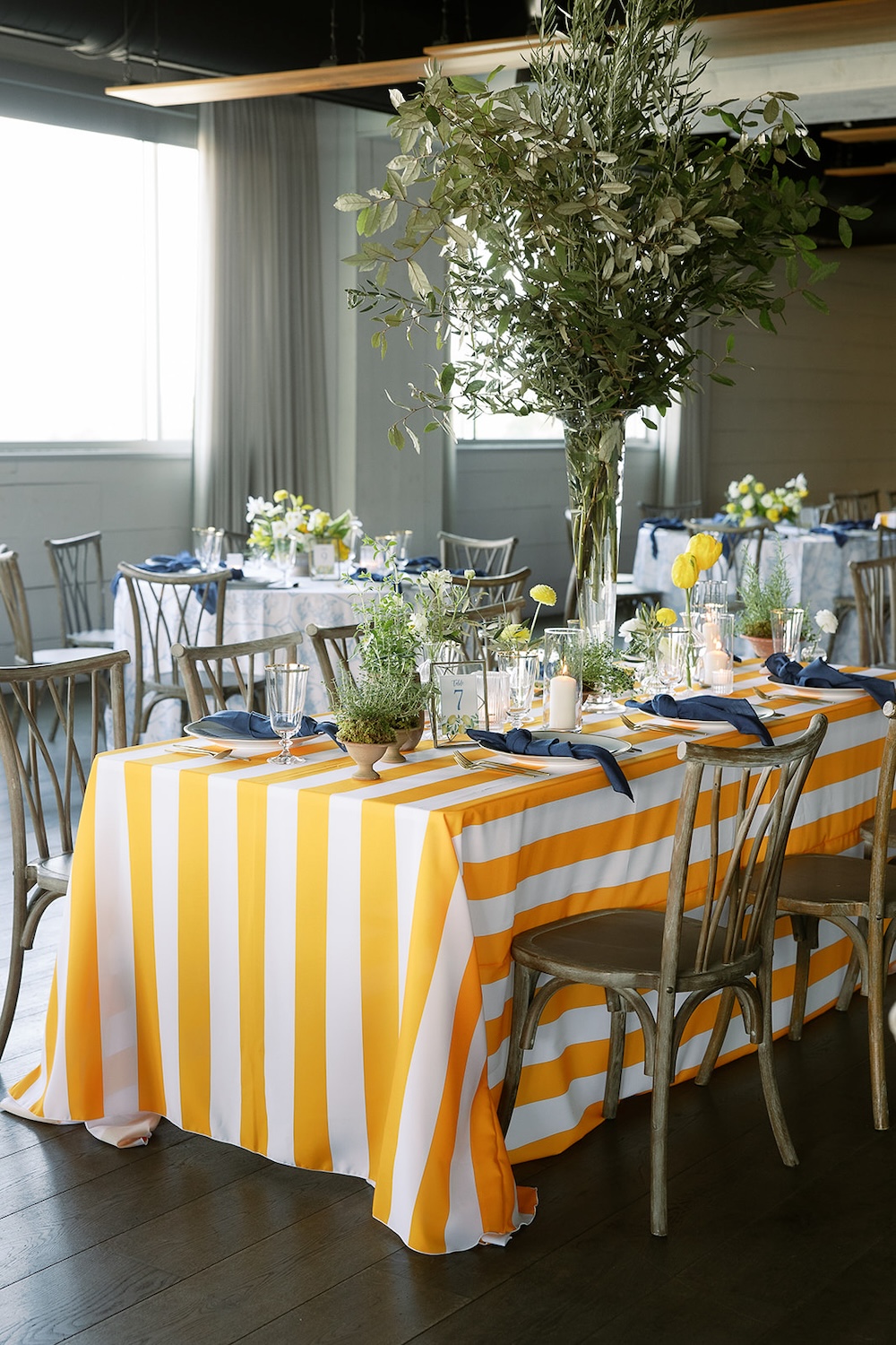 Yellow and white striped table linen with floral centerpieces and olive tree branches.  Italian inspired wedding rehearsal dinner in Greenville, SC. Sarah Bradshaw Photography