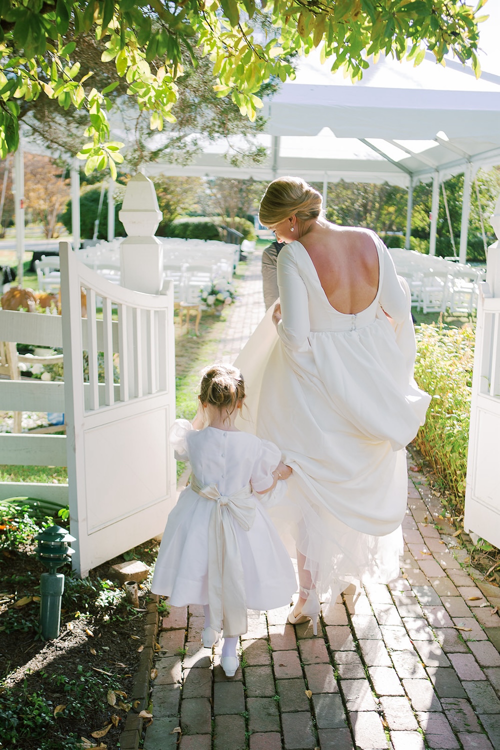 bride and flower girl walk in garden. open back wedding dress with sleeves, no lace. Classic timeless winter wedding, woodlawn manor, alexandria va. Sarah bradshaw photography