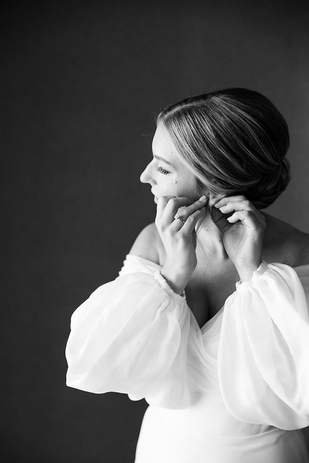 black and white portrait of bride in off shoulders long sleeves wedding dress putting on earrings. High end hotel ballroom wedding, The Fairmont, Washington DC. Sarah Bradshaw Photography