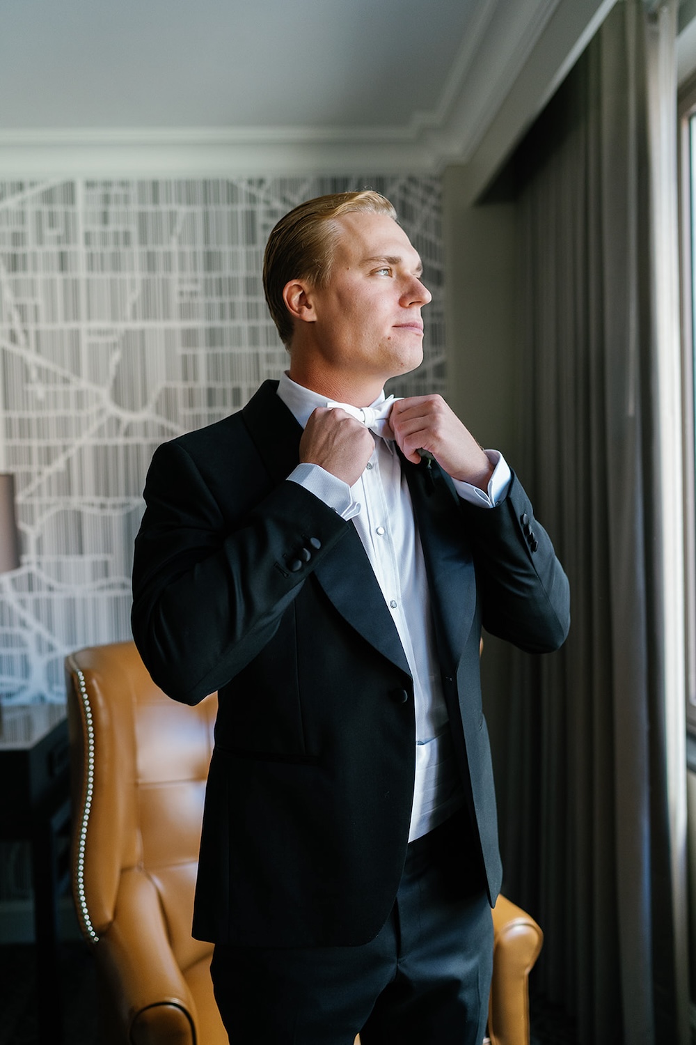 groom adjusts bowtie while wearing tuxedo in modern hotel room. High end hotel ballroom wedding, The Fairmont, Washington DC. Sarah Bradshaw Photography