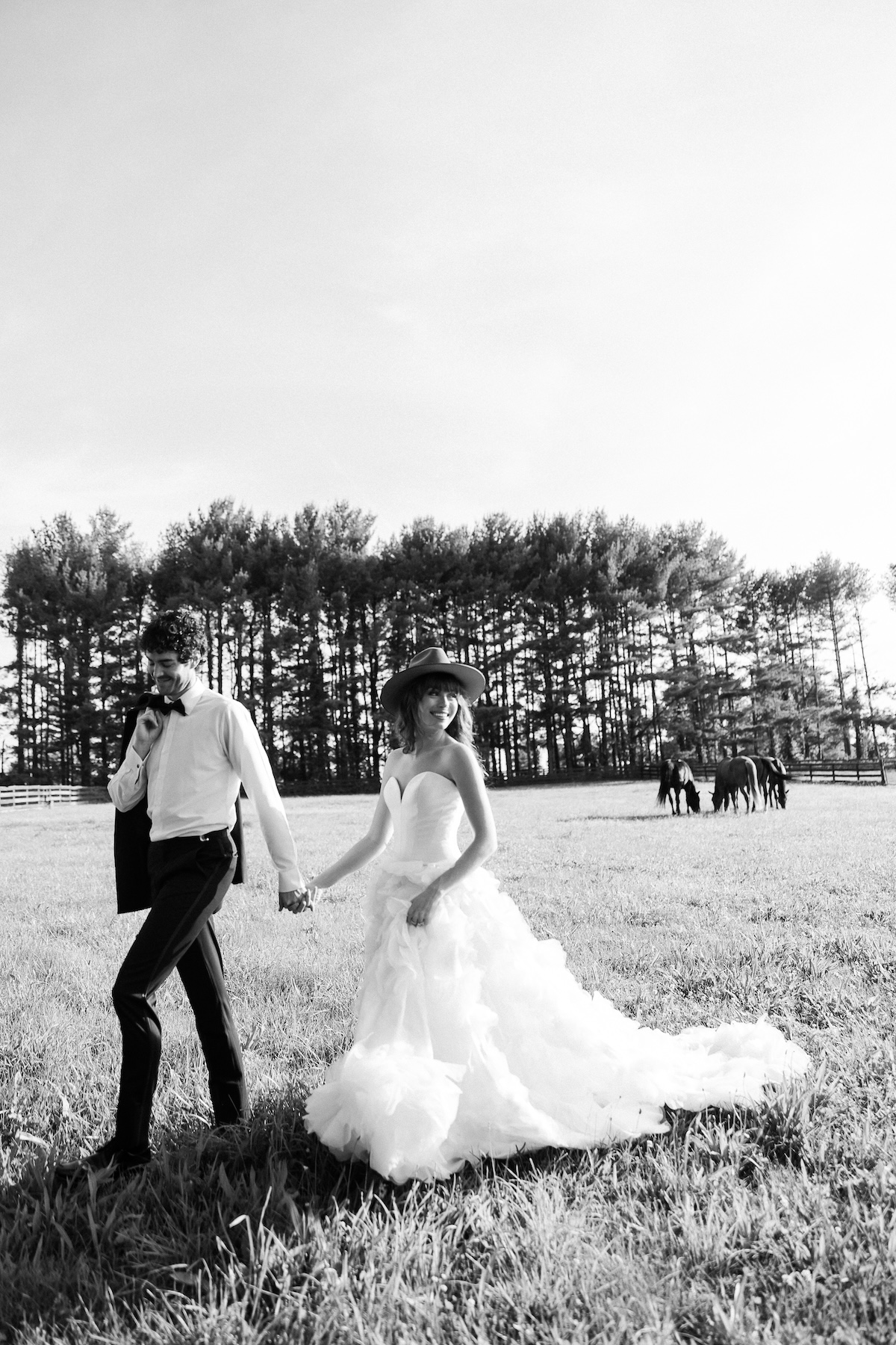 black and white portrait of bride and groom walking in field, horses in background. chic equestrian wedding inspiration at Red Fox Inn, Middleburg Virginia. Sarah Bradshaw